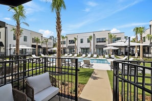 A poolside area with lounge chairs, palm trees, and a modern building with multiple windows. - Cassa Hotel: Luxury Poolside 1BR/2BA Unit 101 (Orlando)