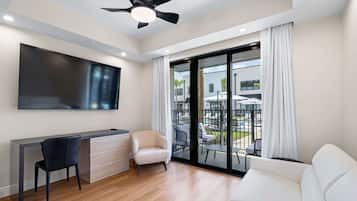 A modern living room with a flat-screen TV, a desk, a chair, a sofa, and a balcony with outdoor furniture.