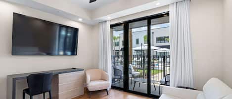Un salon moderne doté d’un téléviseur à écran plat, d’un bureau, d’une chaise, d’un canapé et d’un balcon aménagé avec du mobilier d’extérieur.