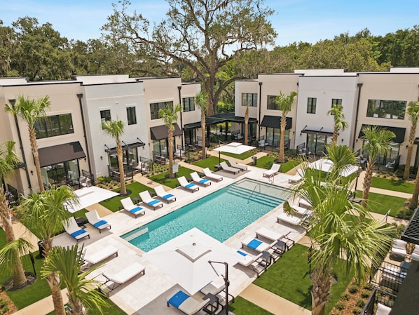 A rooftop pool area with multiple lounge chairs and umbrellas, surrounded by palm trees and modern buildings. - Cassa Hotel: Luxury Poolside 1BR/2BA Unit 101 (Orlando)