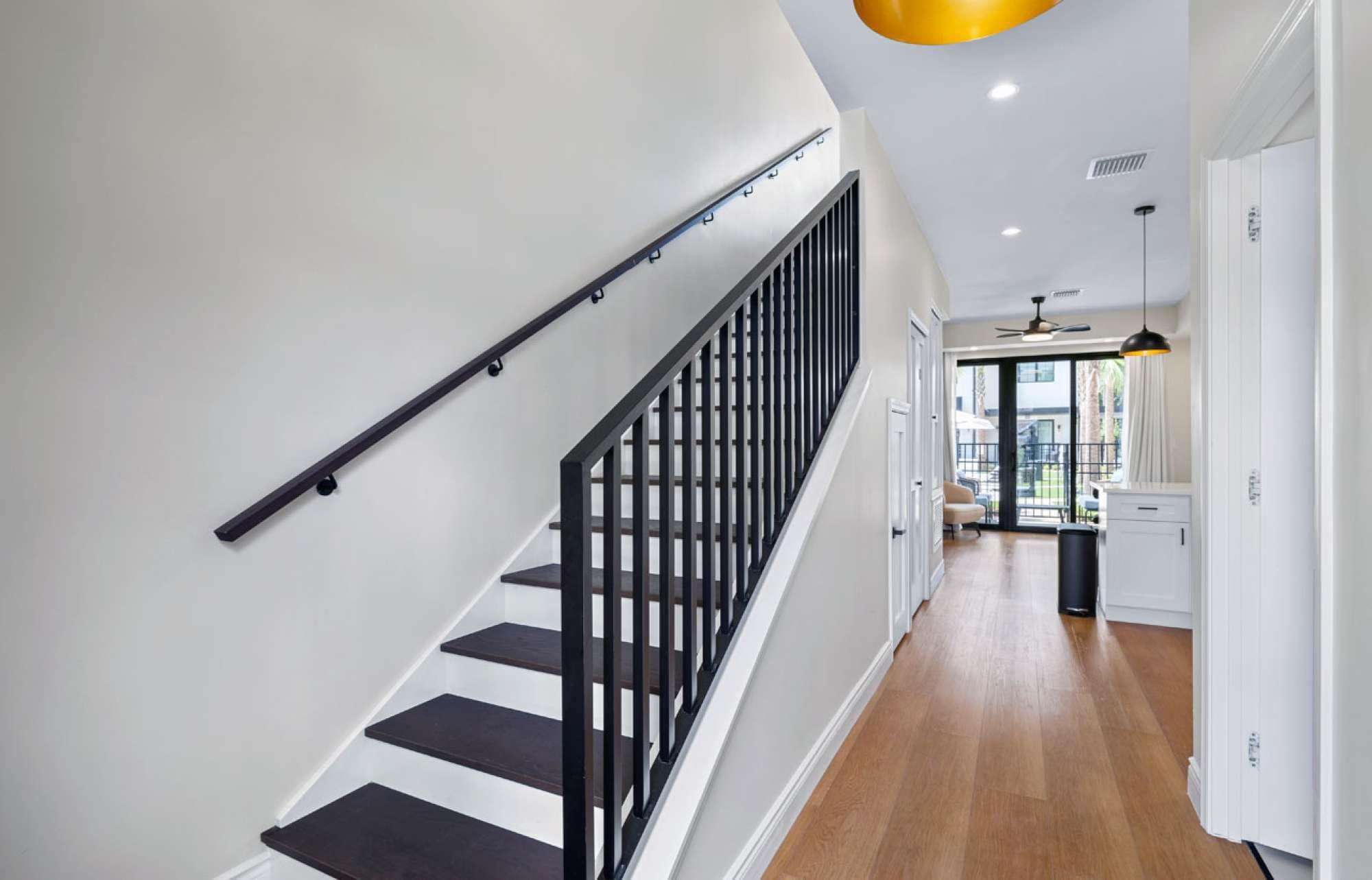 A staircase with black railings leading to a room with a ceiling fan and a view of an outdoor area.