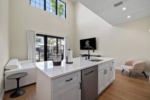 A modern kitchen with a flat-screen TV, a dining area with a white table and chairs, and a view of the outdoors through a large window. - Cassa Hotel: Luxury Poolside 1BR/2BA Unit 101 (Orlando)