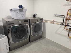 A laundry room with two front-loading washing machines, a dryer, and a water heater. - Shark Belly Mountain Chalet - the Ultimate Lux Mountain Retreat (Bethel)