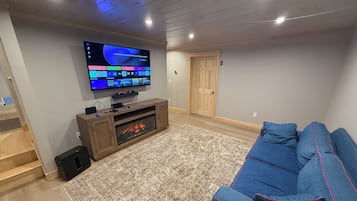 A living room with a flat-screen TV, a wooden entertainment unit, a blue sofa, and a patterned rug.