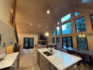 Une cuisine spacieuse avec un grand îlot central, un plafond en bois et de grandes fenêtres.
