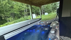 Ett bubbelbad med marmorliknande design, omgivet av ett trädäck, med utsikt över ett skogsområde.