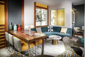 Een moderne woonkamer met een houten eettafel, een blauwe bank, gestreept fauteuils en een salontafel.