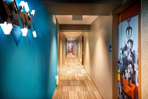 Een hotelgang met een blauwe muur, een houten vloer en een deur met een poster.