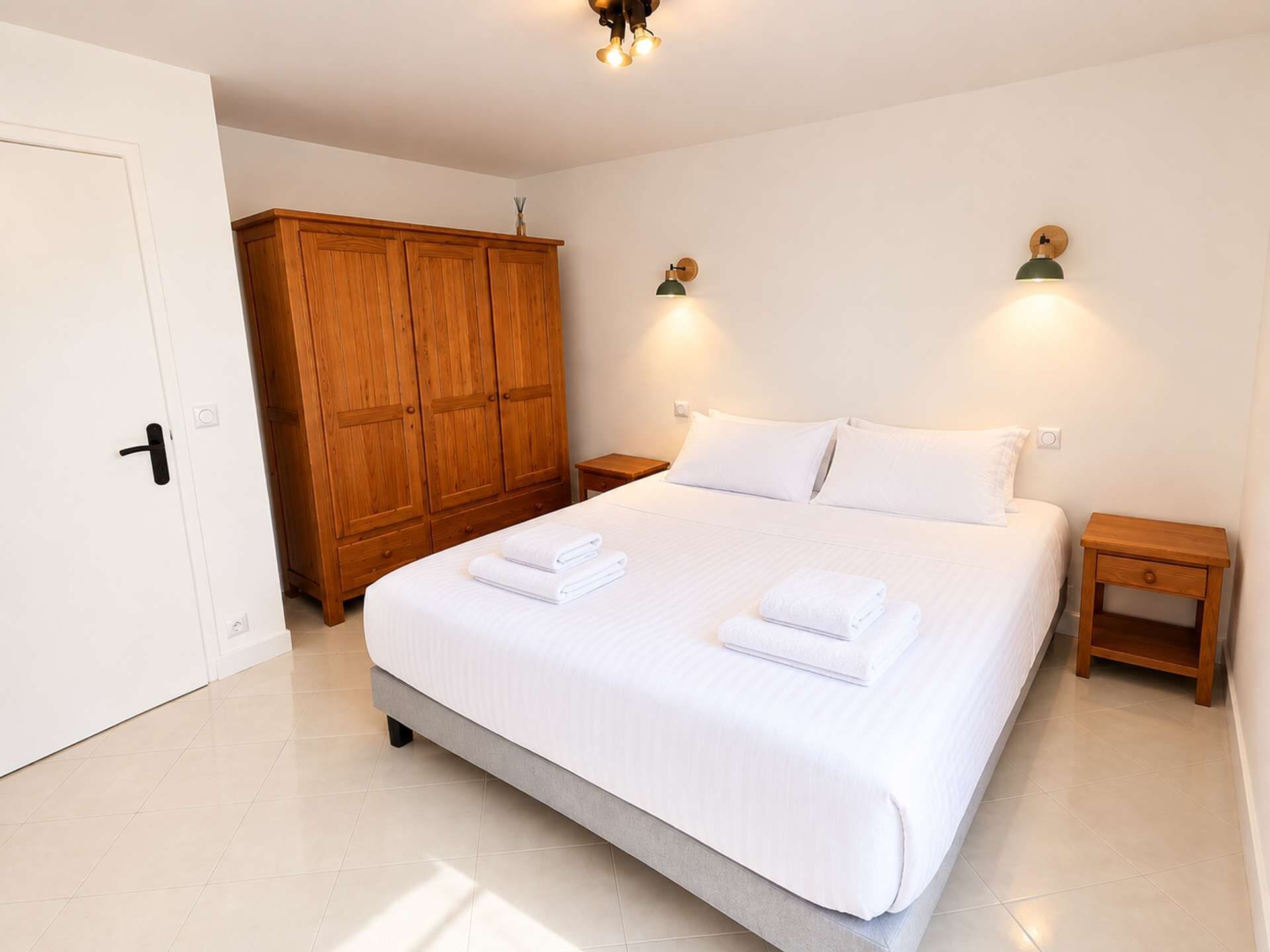 Un dormitorio con una cama grande, un armario de madera, dos mesitas de noche y lámparas de pared.