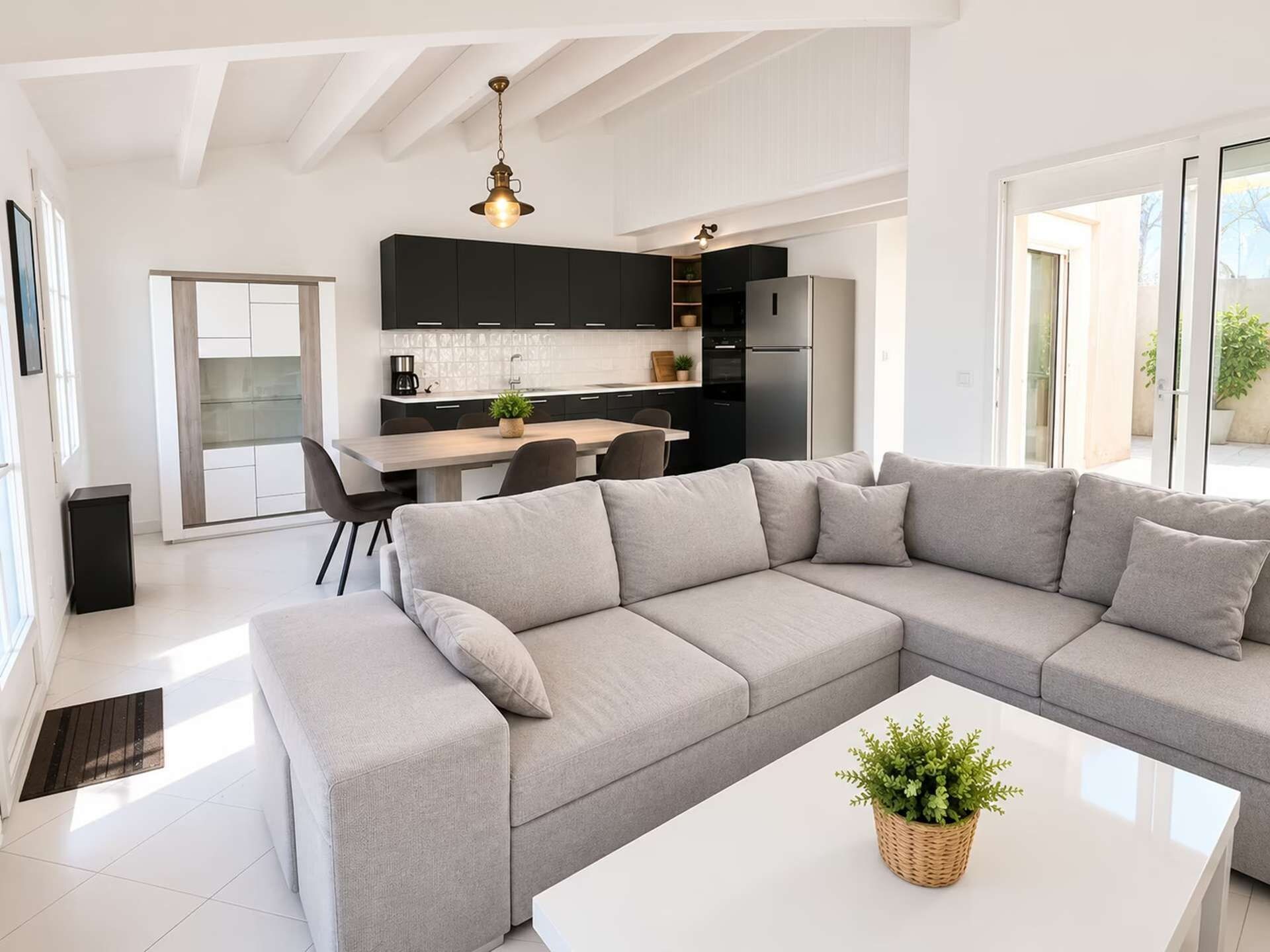 Ein modernes Wohnzimmer mit einem grauen Ecksofa, einem weißen Couchtisch und einer Küche im Hintergrund.