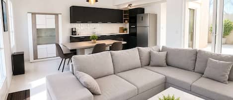 Un salon moderne avec un canapé d’angle gris, une table basse blanche et une cuisine en arrière-plan.