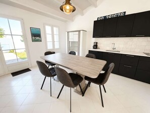 A modern kitchen with a dining table and chairs, a coffee maker, and black cabinets. - Lovely, fully equipped holiday home (LA COUARDE SUR MER)