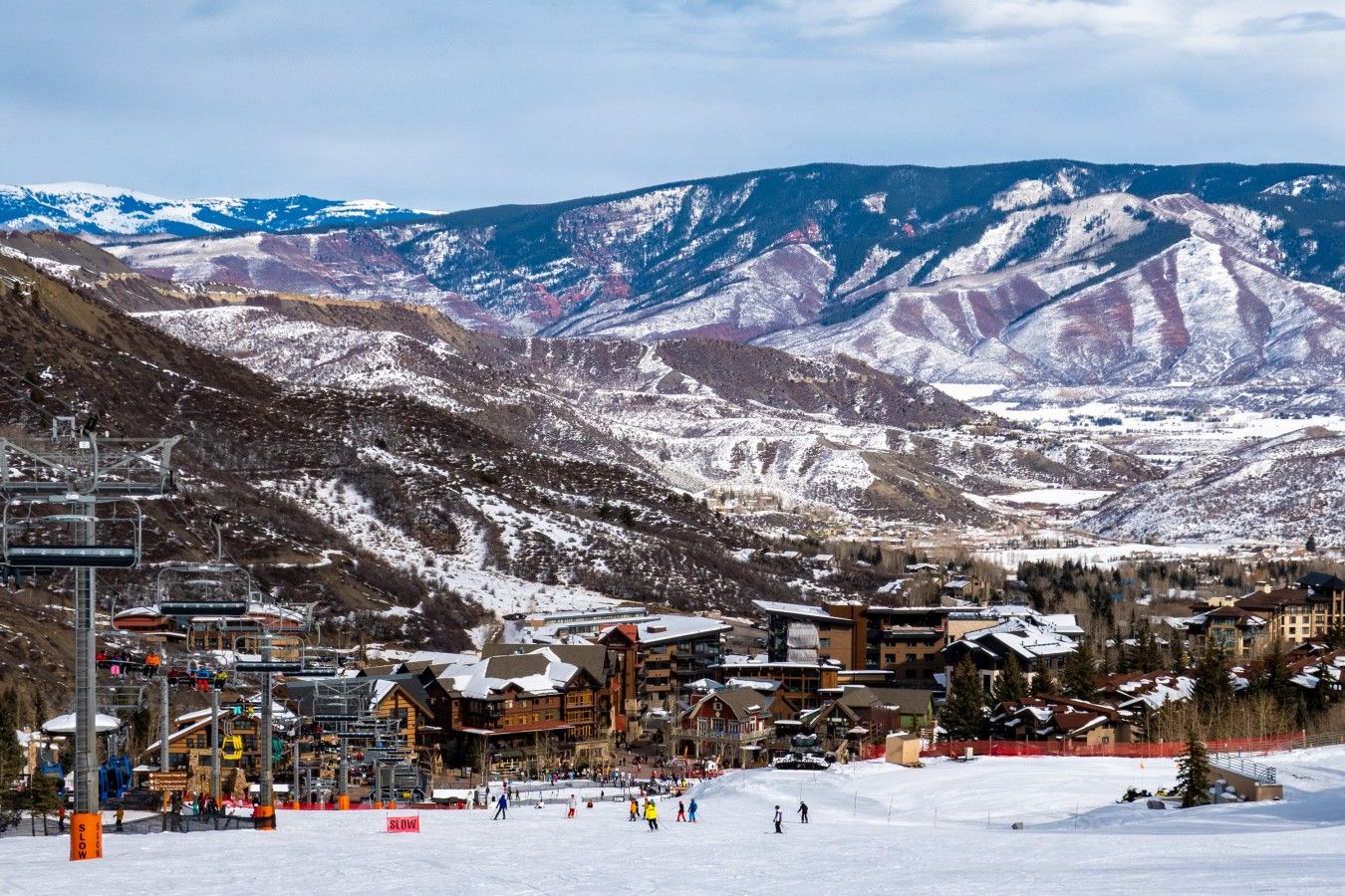 A ski resort with a ski lift, buildings, and snow-covered mountains in the background.