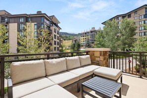 A balcony with a sofa and a table, overlooking a residential area with buildings and trees. - New! 2BR Luxury Retreat – Ski-In/Out + Large Patio (Snowmass Village)