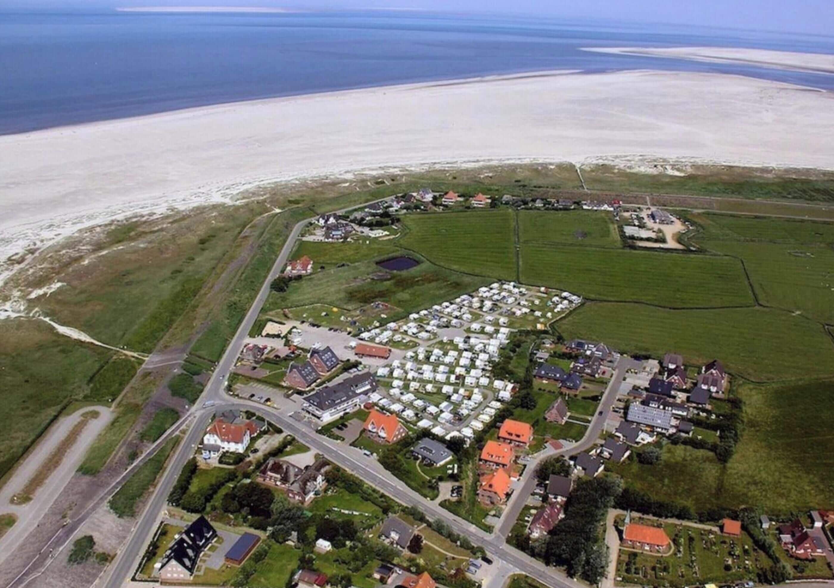An aerial view of a coastal area with a large caravan park, several buildings, and a road network.