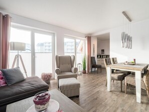 A modern living room with a sofa, ottoman, and dining table. - SPO Beach House 2 (St. Peter-Ording)
