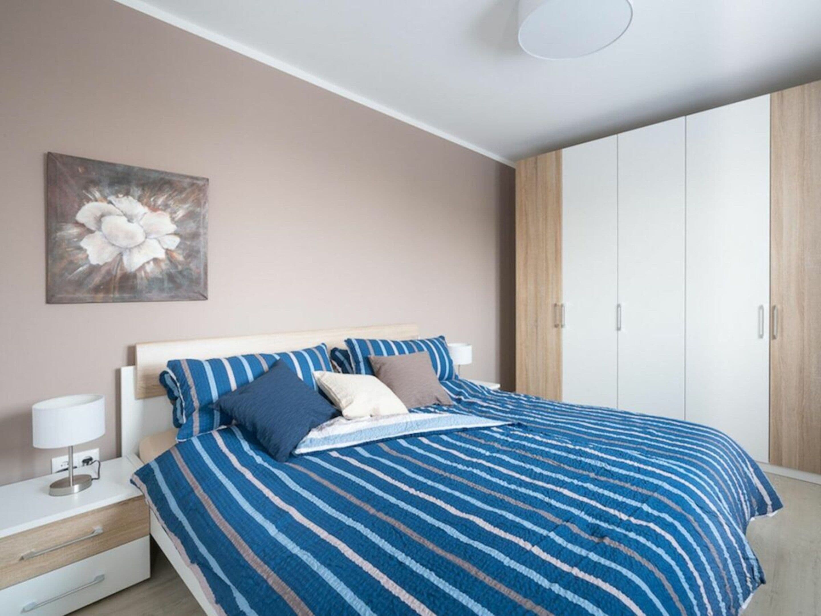 A bedroom with a bed, bedside tables, a lamp, a painting, and a wardrobe.