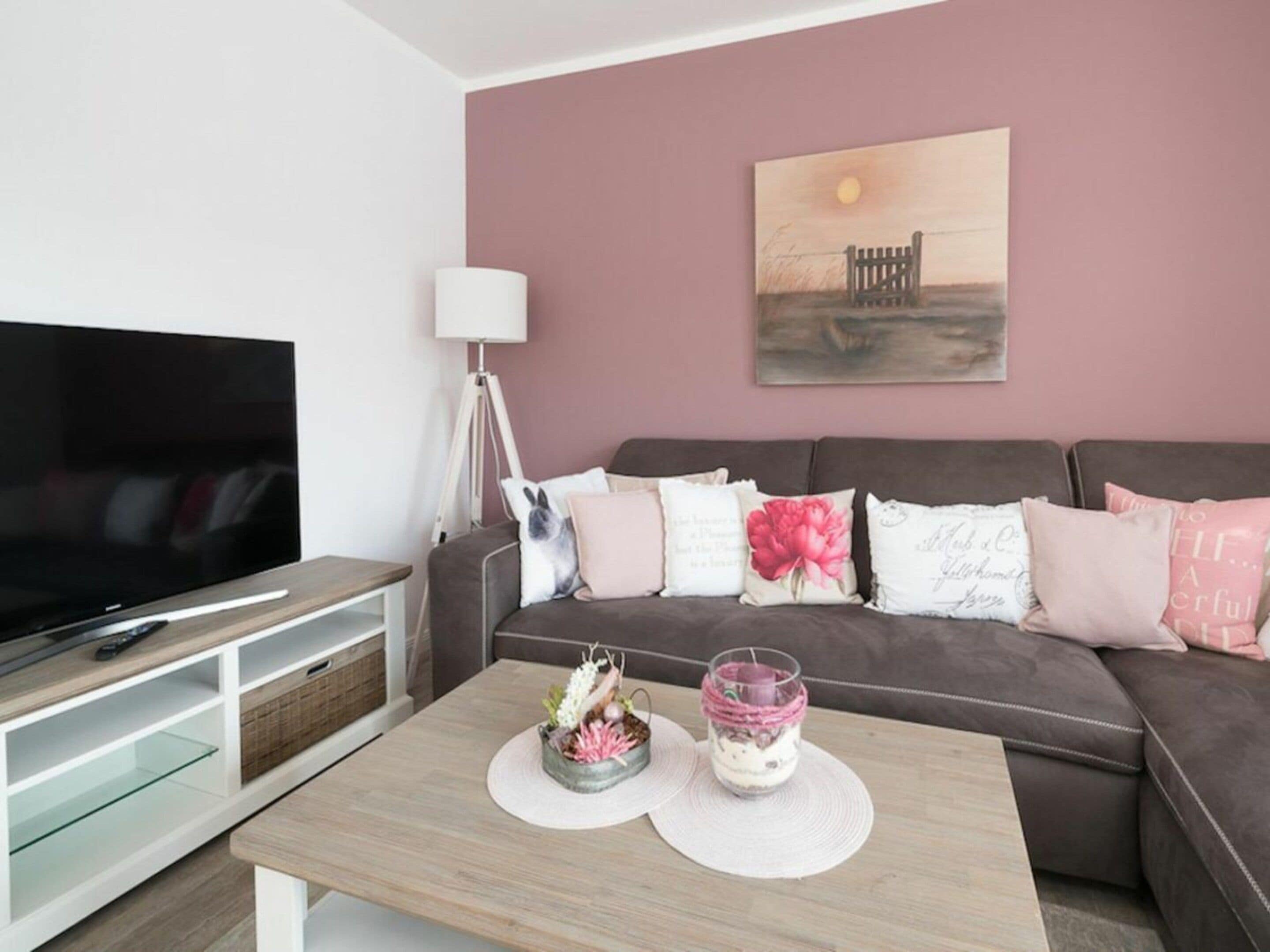 A modern living room with a flat-screen TV, a sofa with decorative pillows, a coffee table with a candle and a small plant, and a painting on the wall.