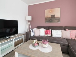 A modern living room with a flat-screen TV, a sofa with decorative pillows, a coffee table with a candle and a small plant, and a painting on the wall. - SPO Beach House 2 (St. Peter-Ording)