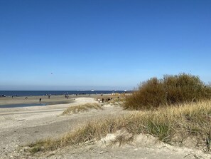 Ein Strand mit Menschen, einem klaren Himmel und einem Schiffen in der Ferne.