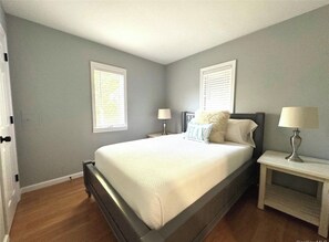 A bedroom with a bed, two bedside tables, and a window with blinds. - Beautiful Home Near Beaches, Restaurants & Local Attractions (Hampton Bays)
