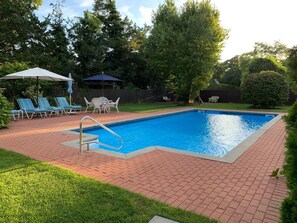 A rectangular swimming pool with a metal ladder, surrounded by a brick patio. There are lounge chairs and a table with umbrellas. - Beautiful Home Near Beaches, Restaurants & Local Attractions (Hampton Bays)