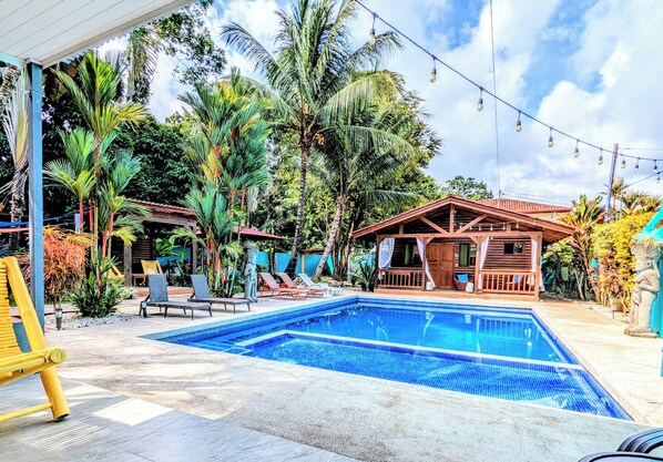 A swimming pool with lounge chairs, surrounded by palm trees and a wooden structure.