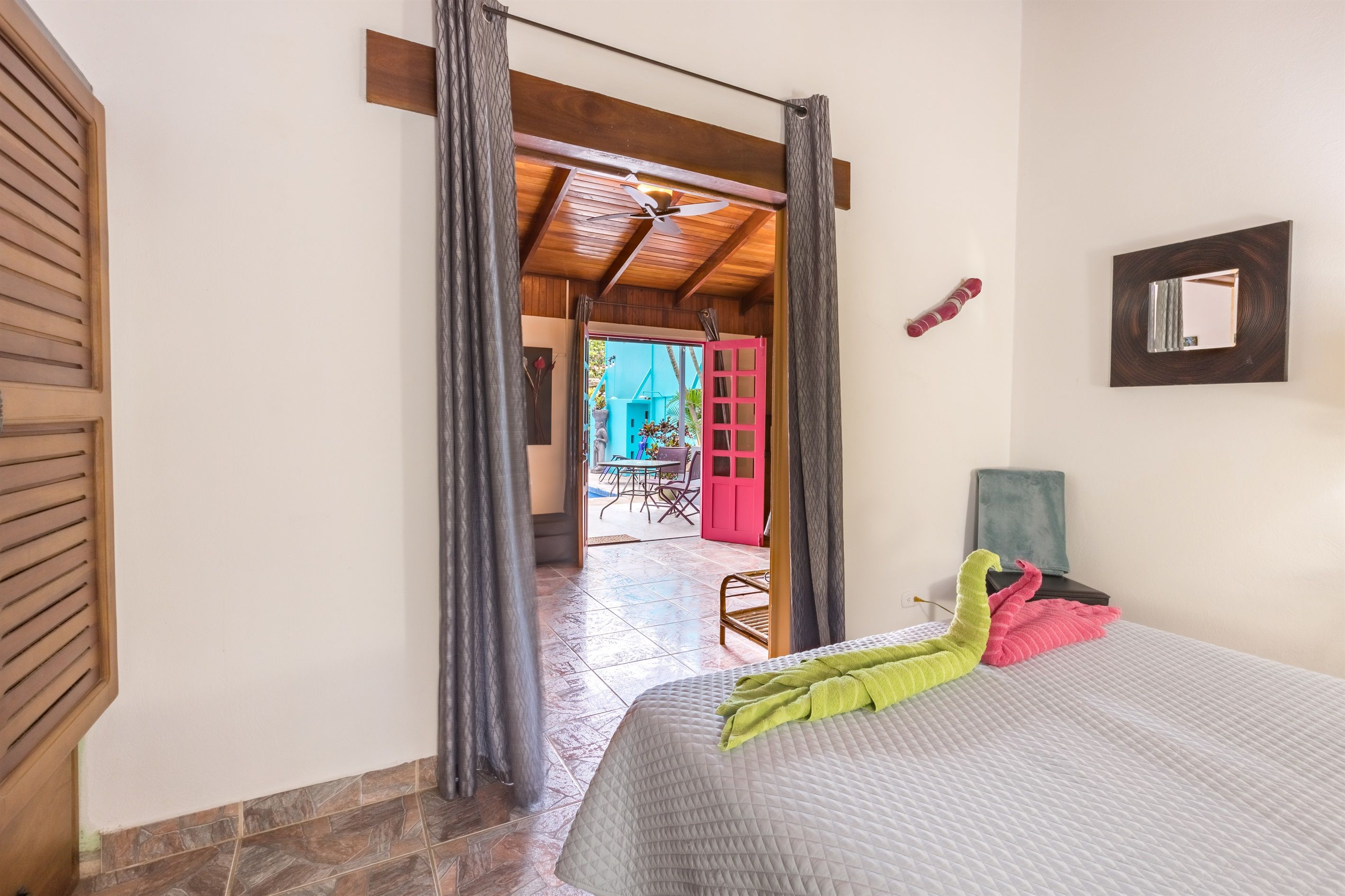 A hotel room with a bed, a ceiling fan, a view of the outside, and a door leading to a balcony.