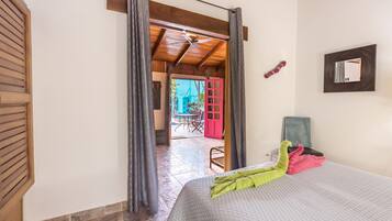 A hotel room with a bed, a ceiling fan, a view of the outside, and a door leading to a balcony.