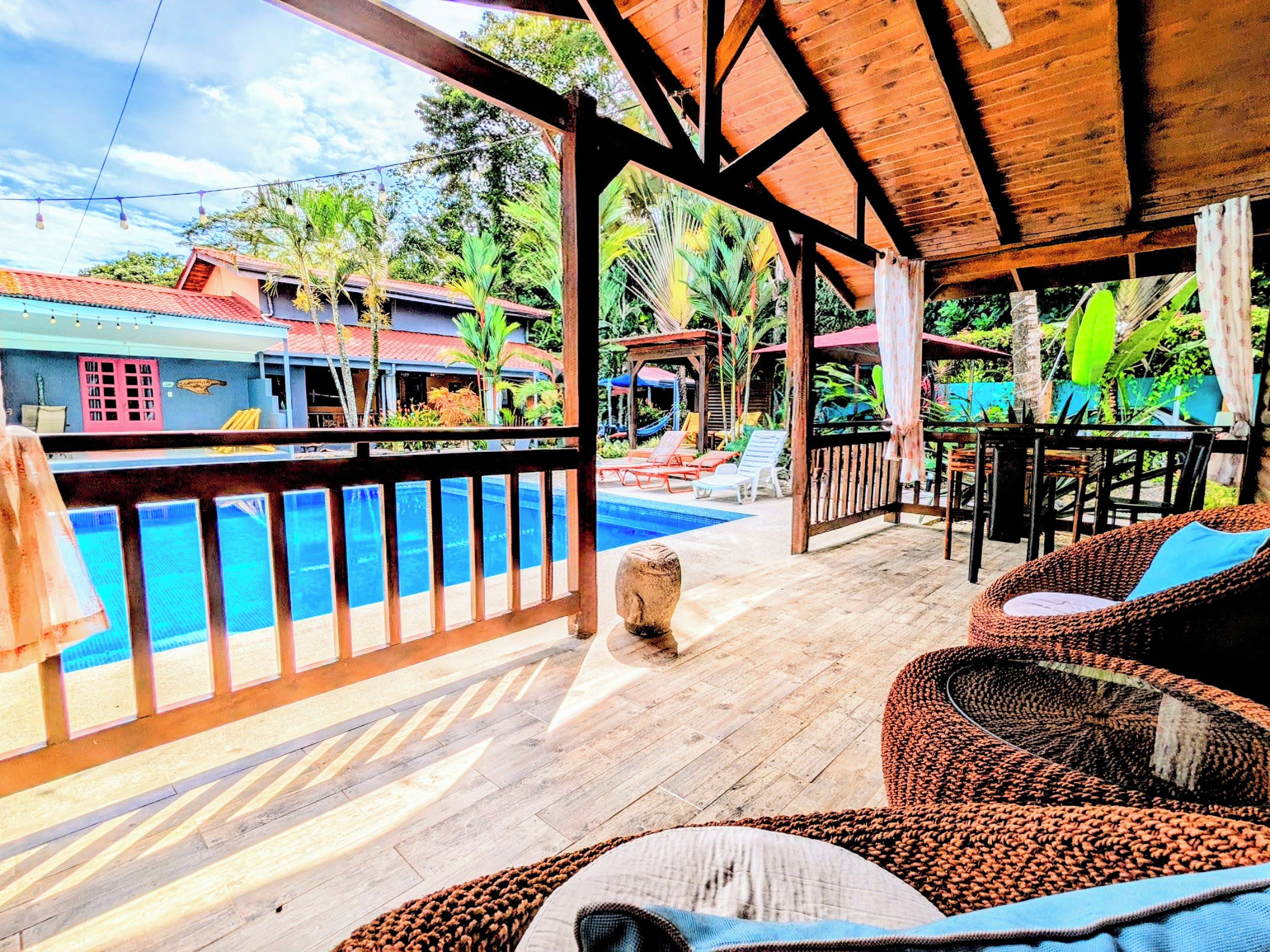 Una terraza de madera con piscina, sillas de descanso y vistas a un paisaje tropical.