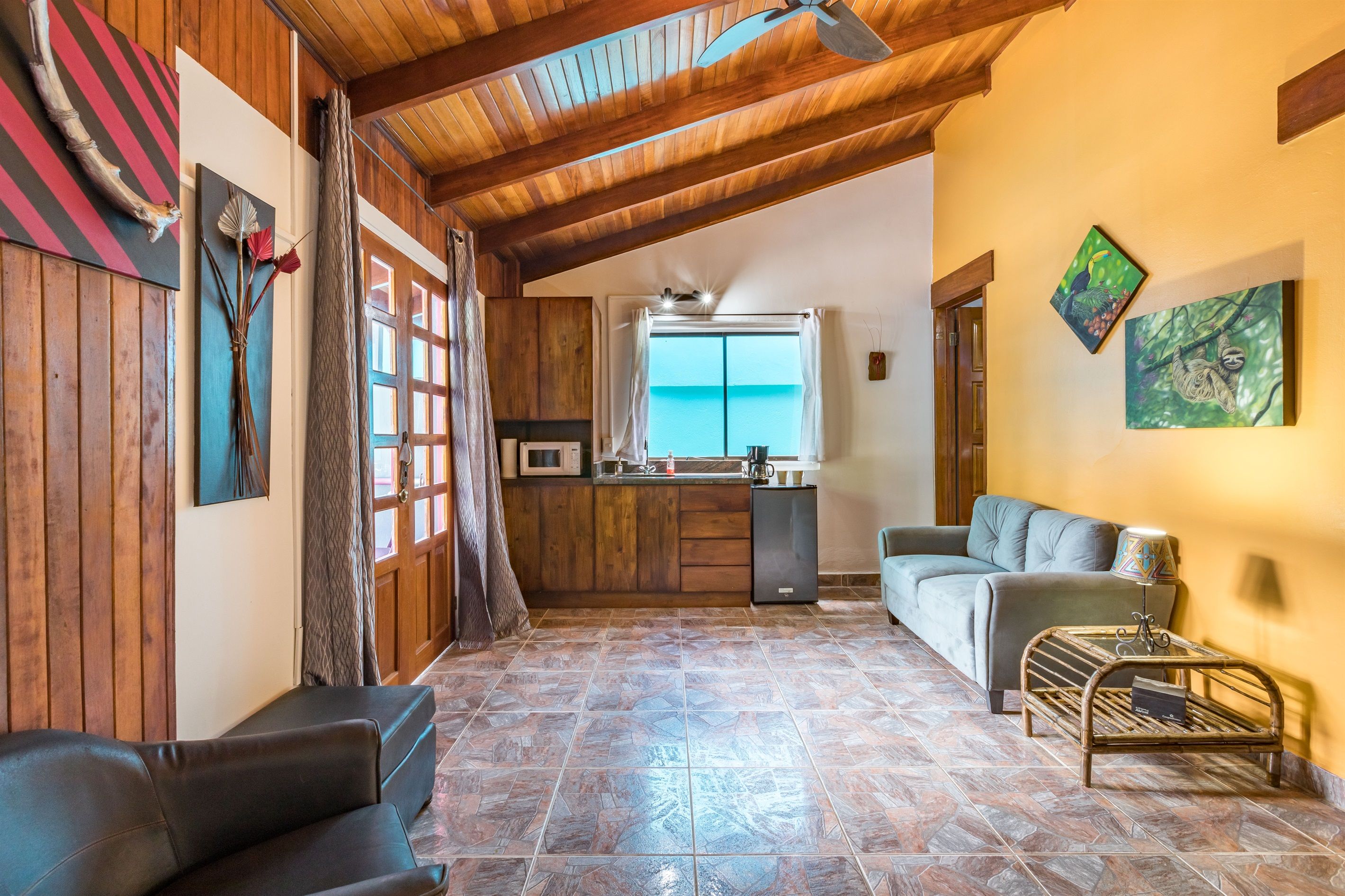 Un espacio de sala acogedor con techo de madera, un sofá, una mesita de centro y una cocina al fondo.