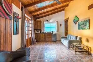 A cozy living area with a wooden ceiling, a sofa, a coffee table, and a kitchen in the background.