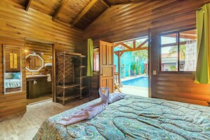 A wooden room with a bed, a bathroom, and a view of a swimming pool.