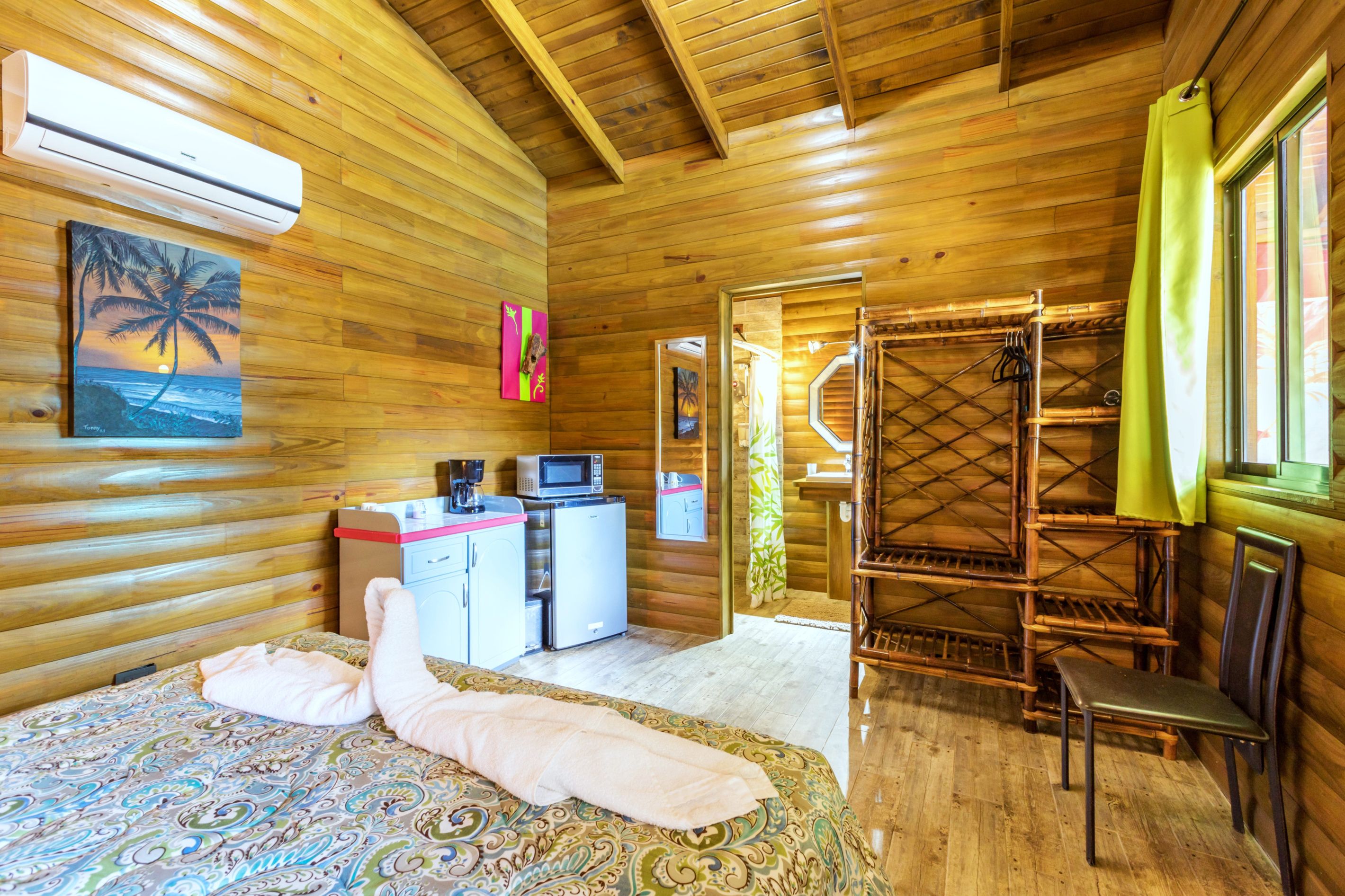 Une chambre dans un chalet en bois, comprenant un lit, un coin cuisine, une zone douche et une fenêtre avec des rideaux.