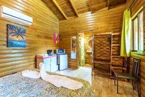 Een houten kamer met een bed, een kitchenette, een douchegedeelte en een raam met gordijnen.