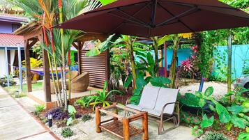 A garden with a wooden bench, a large umbrella, and various tropical plants.