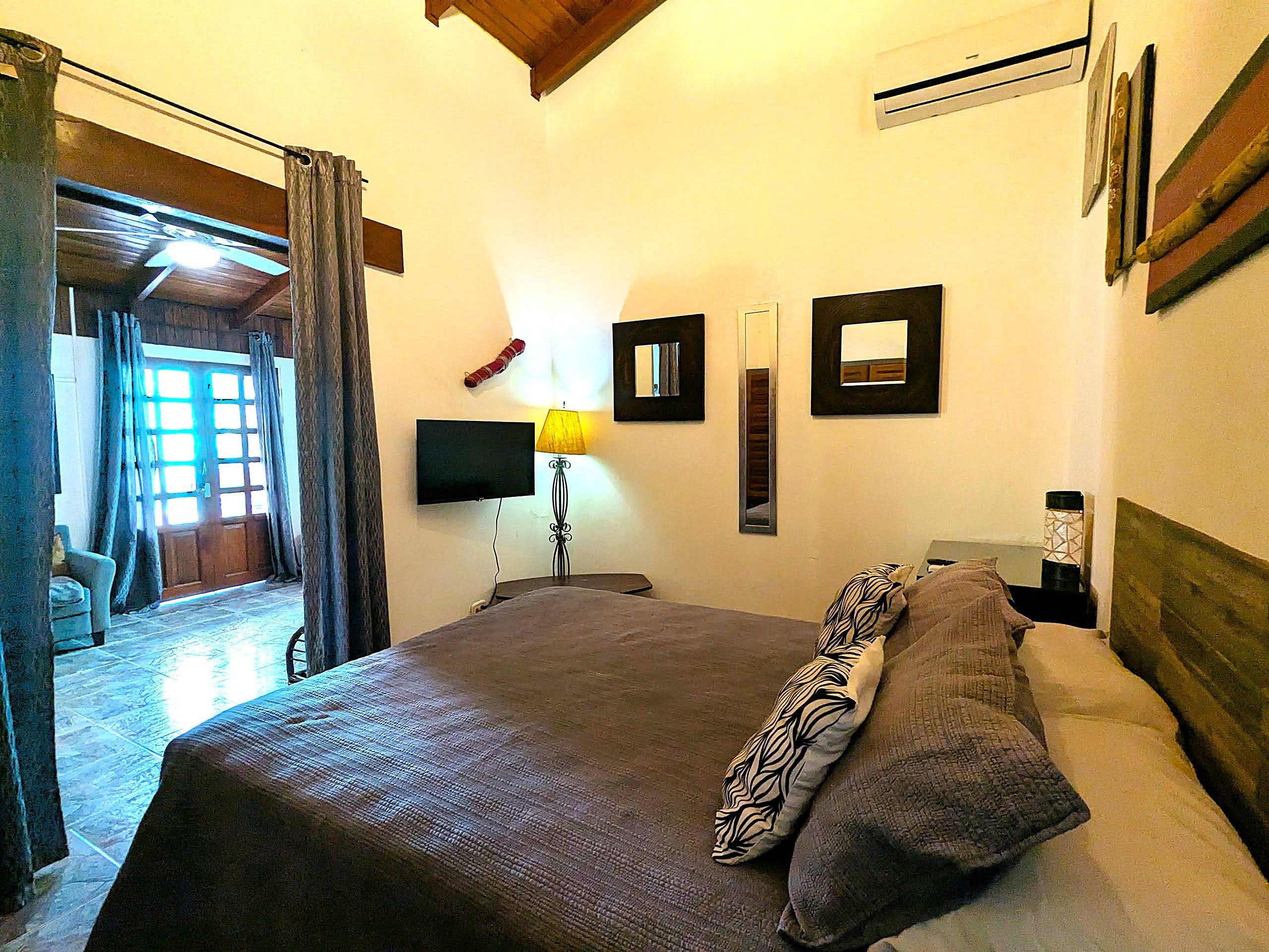 Een slaapkamer met een bed, een televisie, een lamp en een deur naar een balkon.
