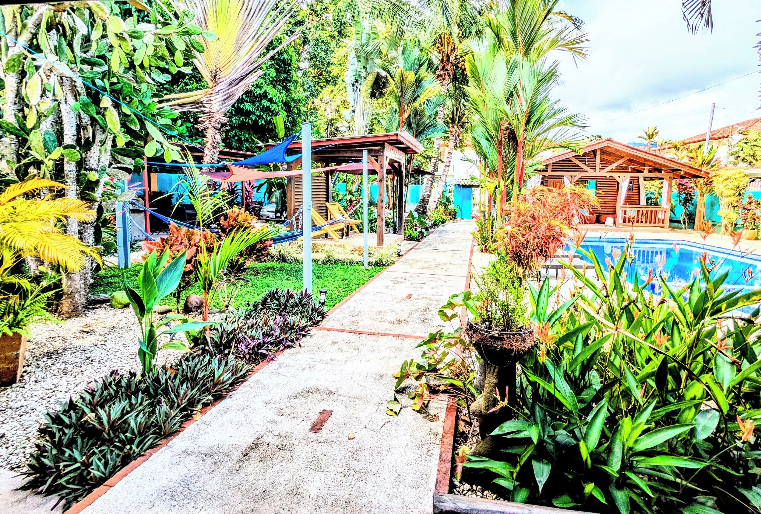 A pathway leading to a pool area surrounded by lush tropical plants and wooden structures.