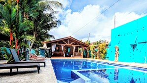 A swimming pool with a wooden deck, lounge chairs, and a building with a porch. - Tropical Paradise w/ 2 Sapacious Cabinas AC & Pool (Playa Herradura)
