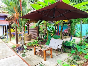 A garden with a wooden bench, a large umbrella, and various tropical plants.