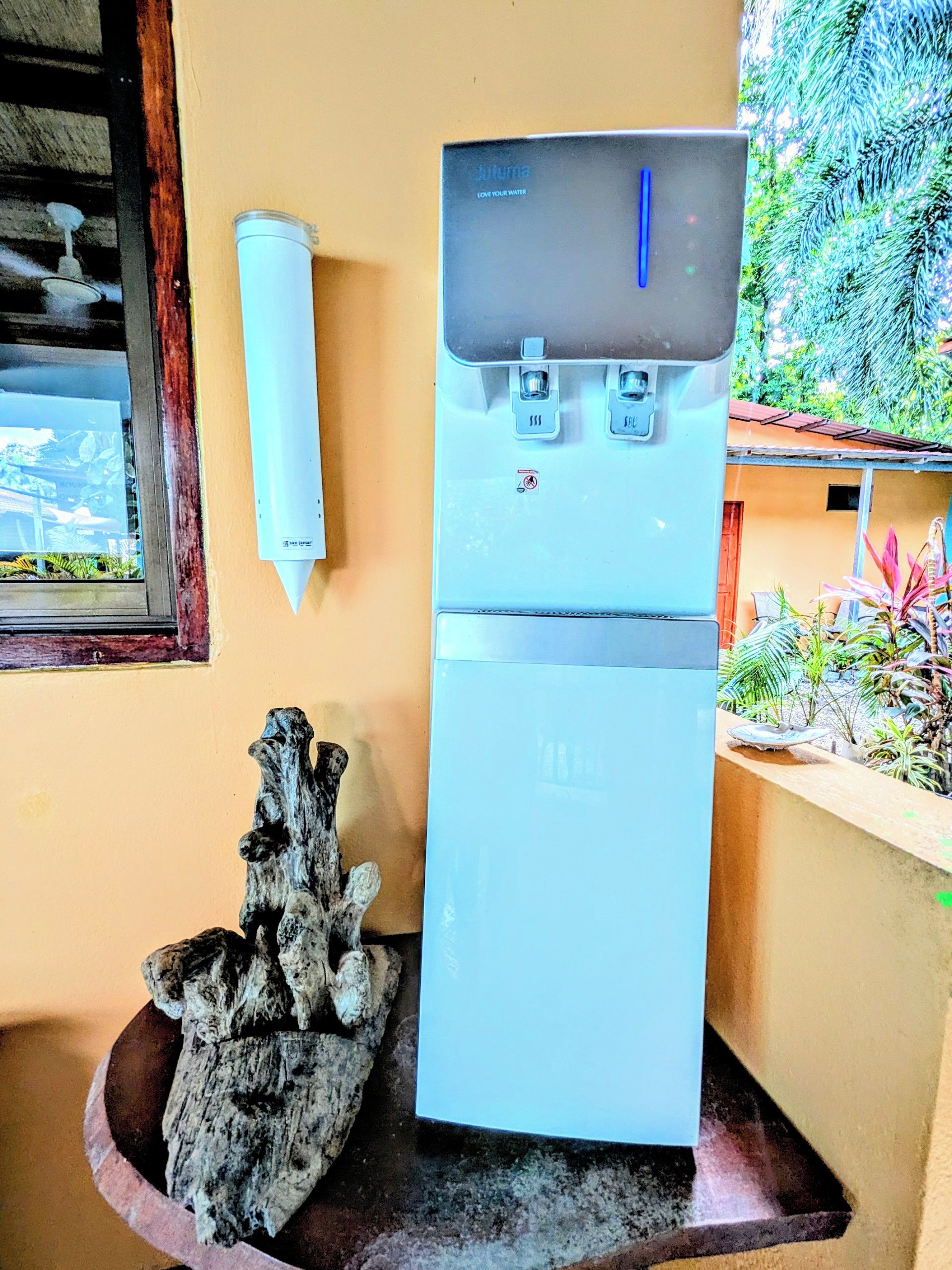 Un dispensador de agua con un panel de control, una escultura de madera y una ventana con vistas a la vegetación.