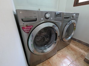 A front-loading LG Direct Drive 20.0kg washer and dryer unit in a laundry room with tiled flooring and a window above the machines. - Stylish & Cozy Private Rooms in Tropical Paradise (Playa Herradura)