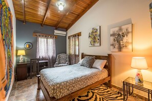 Een slaapkamer met een bed, een bureau, een stoel, een vloerkleed met zebraprint en kunstwerken aan de muren.