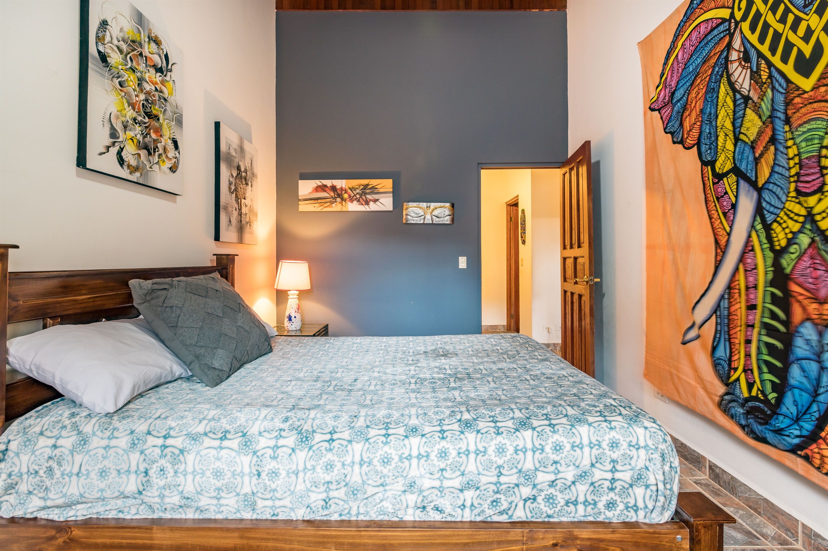 Un dormitorio con cama, mesita de noche, lámpara y un tapiz de pared grande.