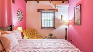 A bedroom with a bed, a chair, a window with blinds, a lamp, and a wall-mounted air conditioner.