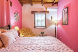 A bedroom with a bed, a chair, a window with blinds, a lamp, and a wall-mounted air conditioner. - Stylish & Cozy Private Rooms in Tropical Paradise (Playa Herradura)