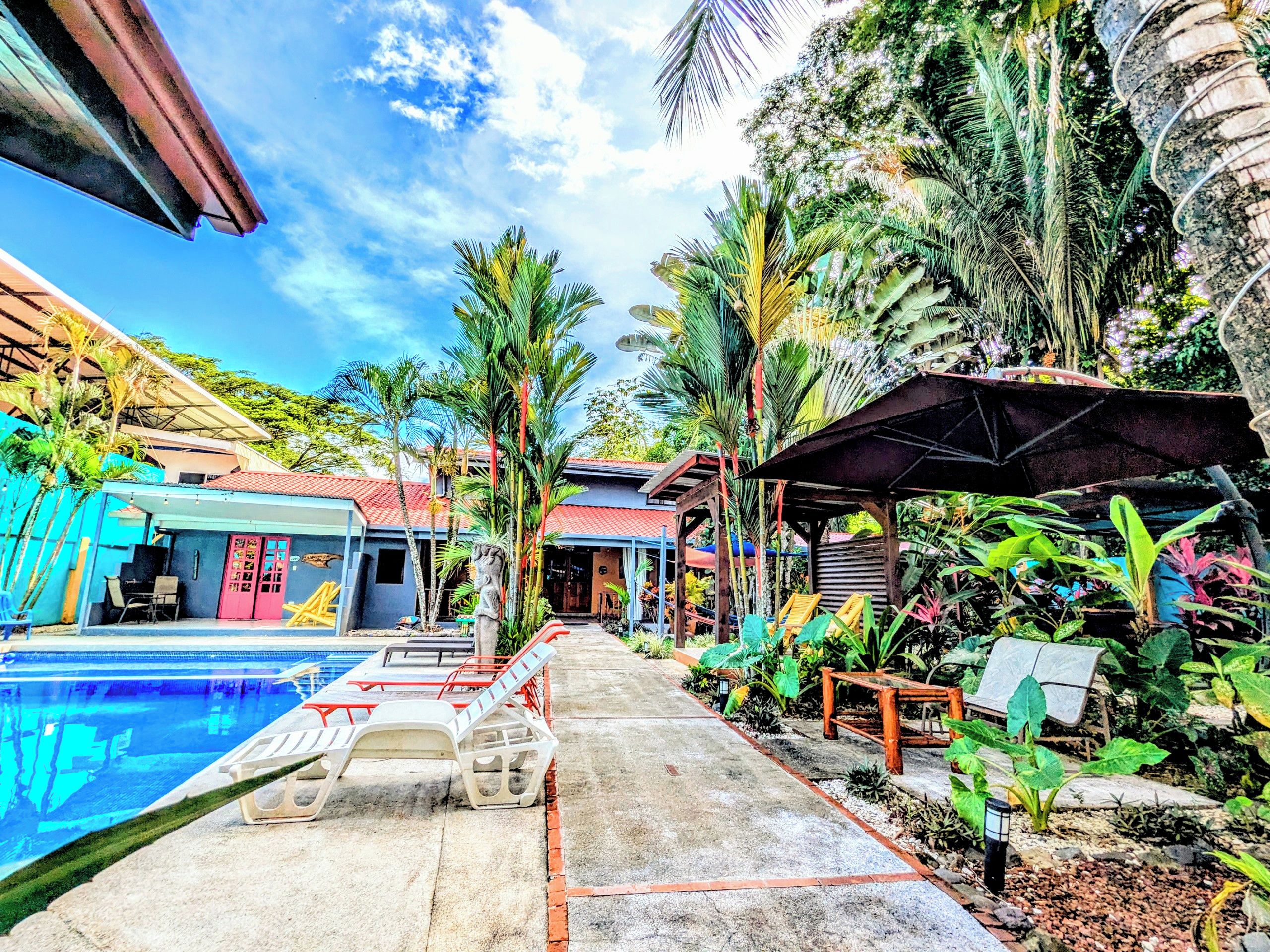 Un'area piscina con lettini, una zona relax coperta e piante tropicali.