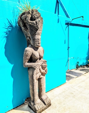 A stone statue of a figure with a plant on its head, standing against a bright blue wall. - Stylish & Cozy Private Rooms in Tropical Paradise (Playa Herradura)