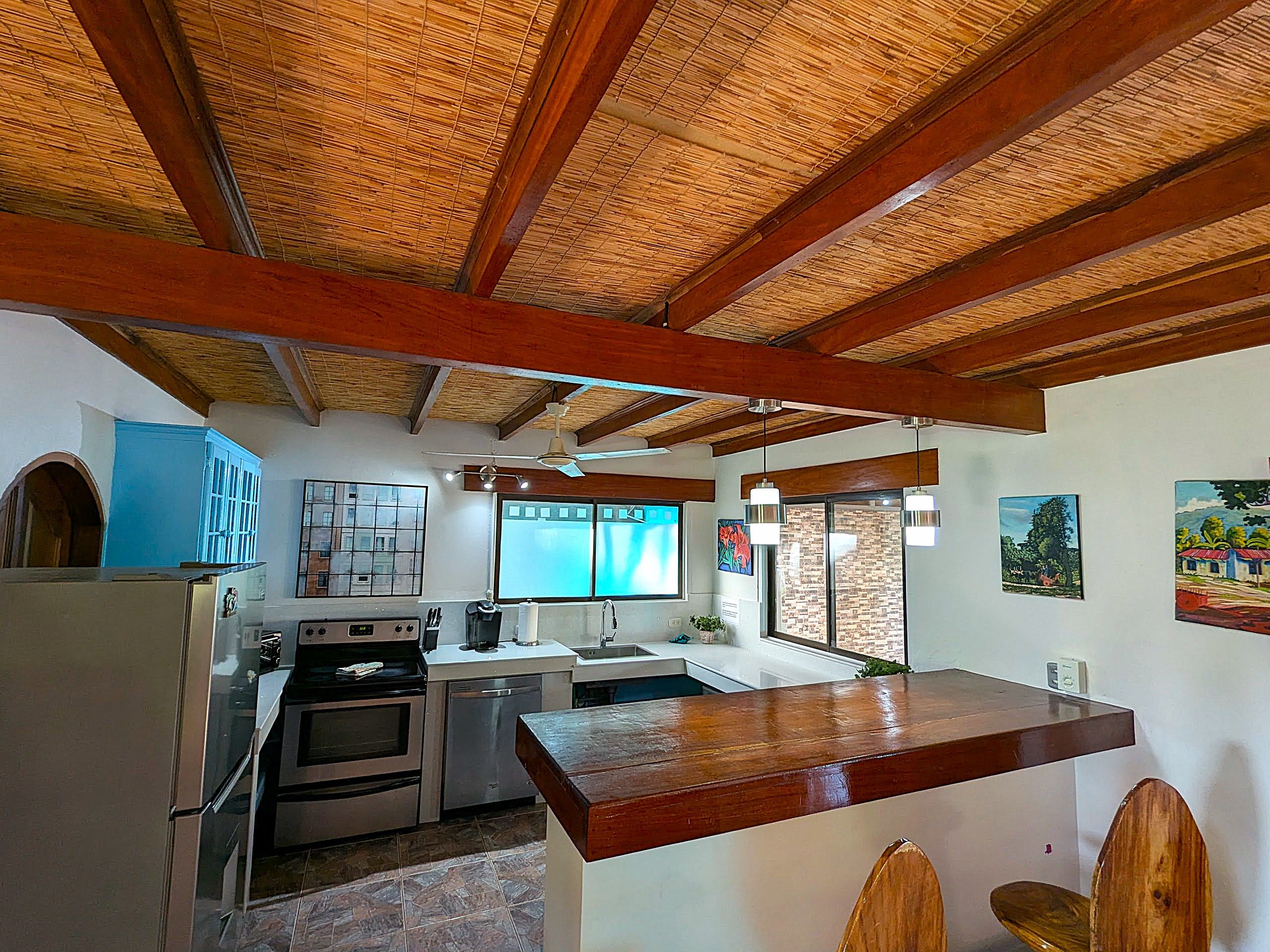 Una cocina con techo de madera, un refrigerador, un horno, un lavamanos y una ventana.