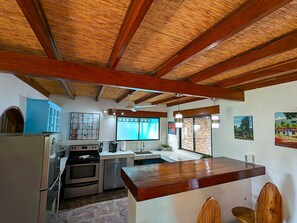 A kitchen with a wooden ceiling, a refrigerator, an oven, a sink, and a window.